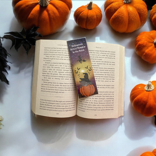 Open book with a Halloween-themed bookmark surrounded by small pumpkins on a white surface.