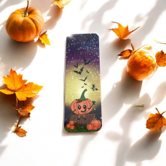 Bookmark with pumpkin design surrounded by pumpkins and leaves on a white surface