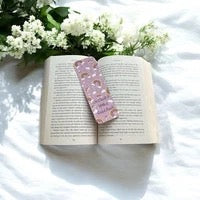 Open book with a pink floral bookmark on a white surface with flowers
