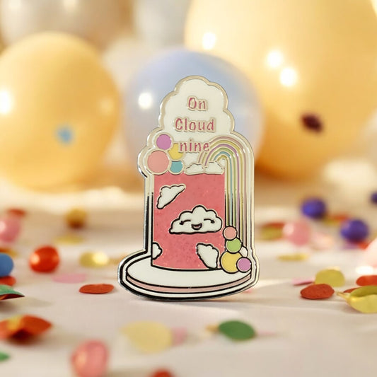 On Cloud Nine Enamel Pin featuring pink glitter cake with vibrant rainbow and cloud design - Quirky collectible accessory with dual pin backing