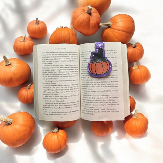 Open book with a pumpkin-shaped bookmark surrounded by small pumpkins on a white background