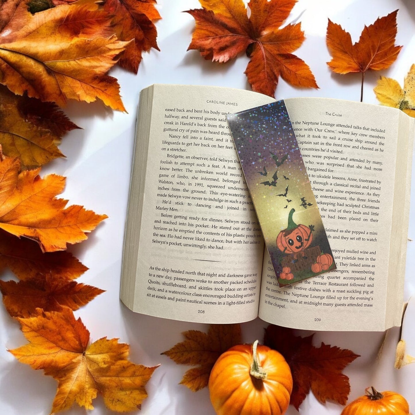 Open book with a Halloween-themed bookmark surrounded by autumn leaves and pumpkins.