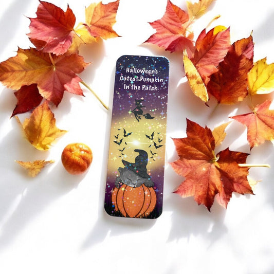 Halloween-themed bookmark with a cat on a pumpkin surrounded by autumn leaves and a small pumpkin.
