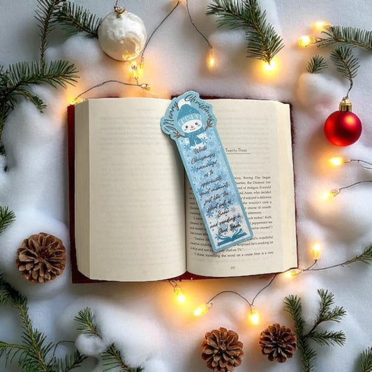 Open book with a Christmas-themed bookmark surrounded by festive decorations on a snowy background.