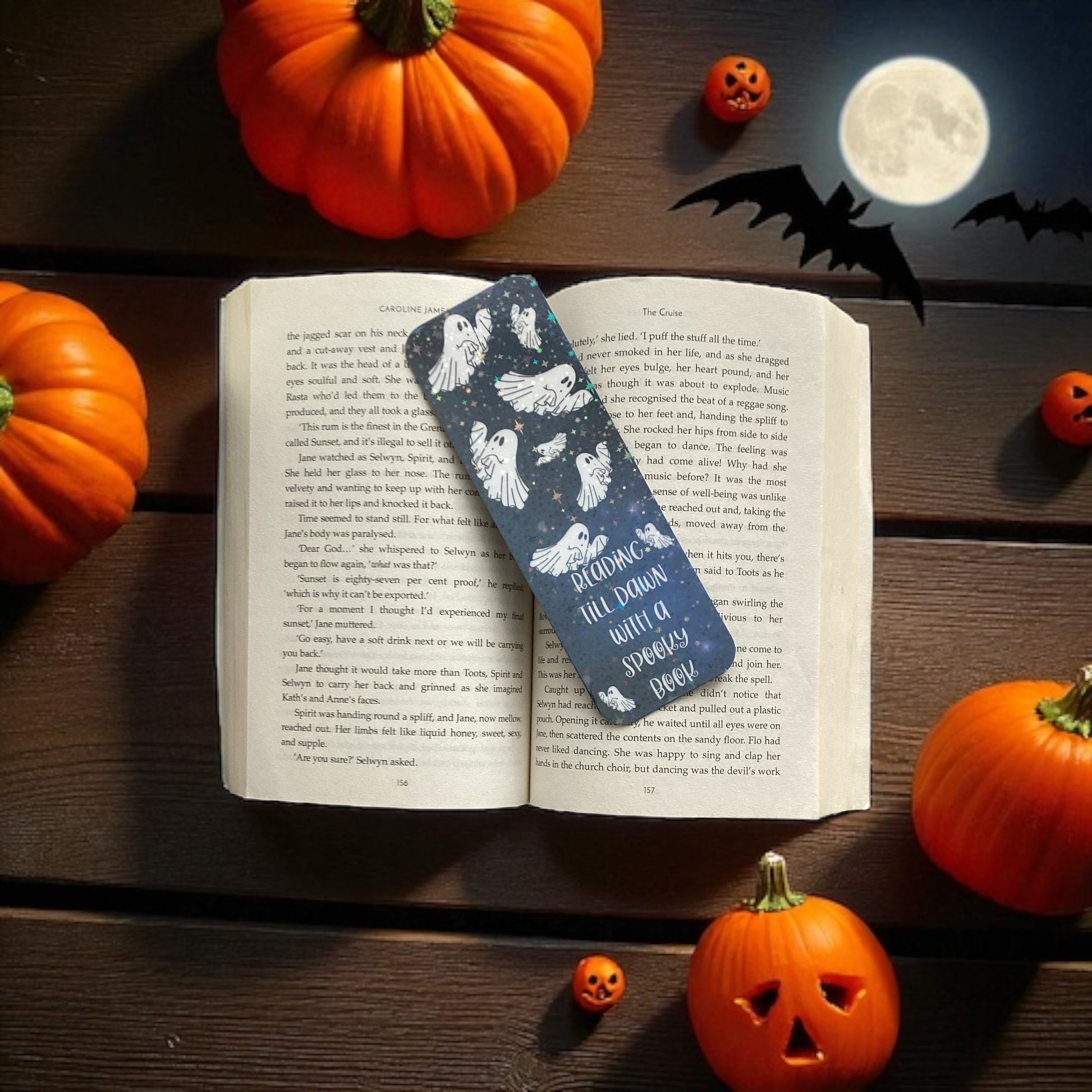Open book with a Halloween-themed bookmark surrounded by pumpkins and a moonlit night scene.