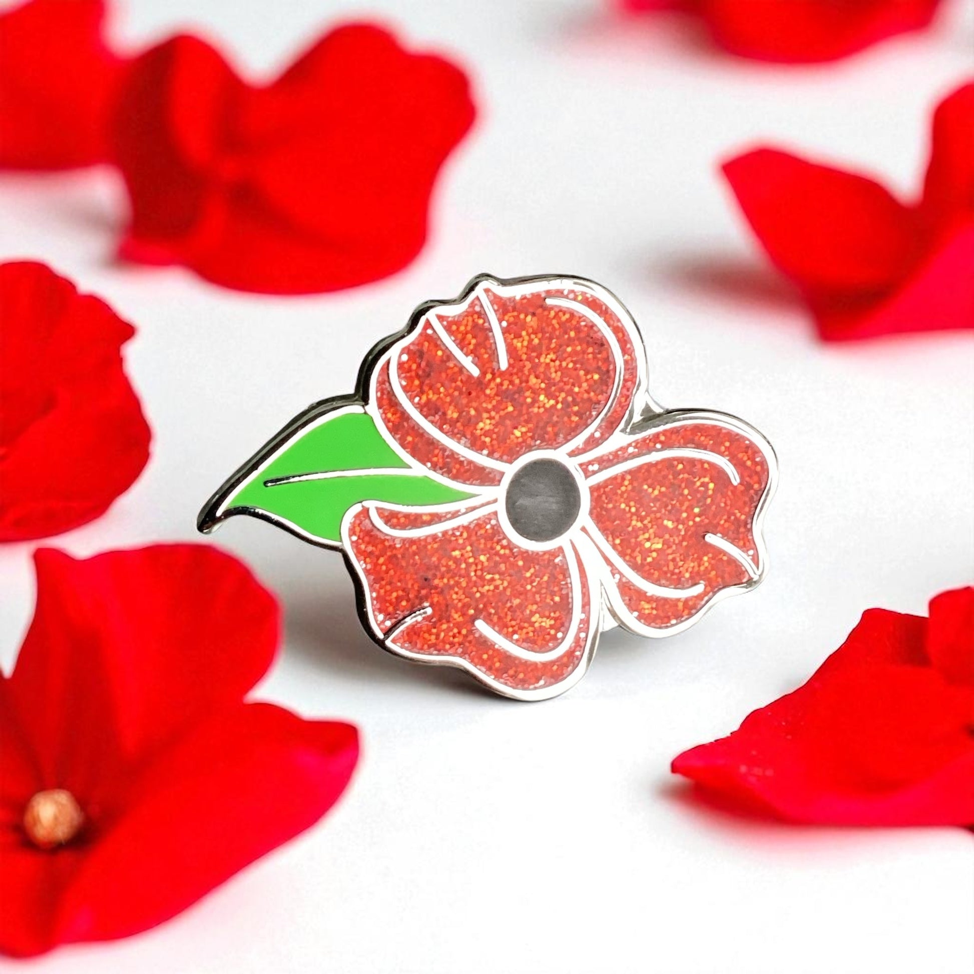Floral pin with red glittery petals and a green leaf on a white background with red flowers.