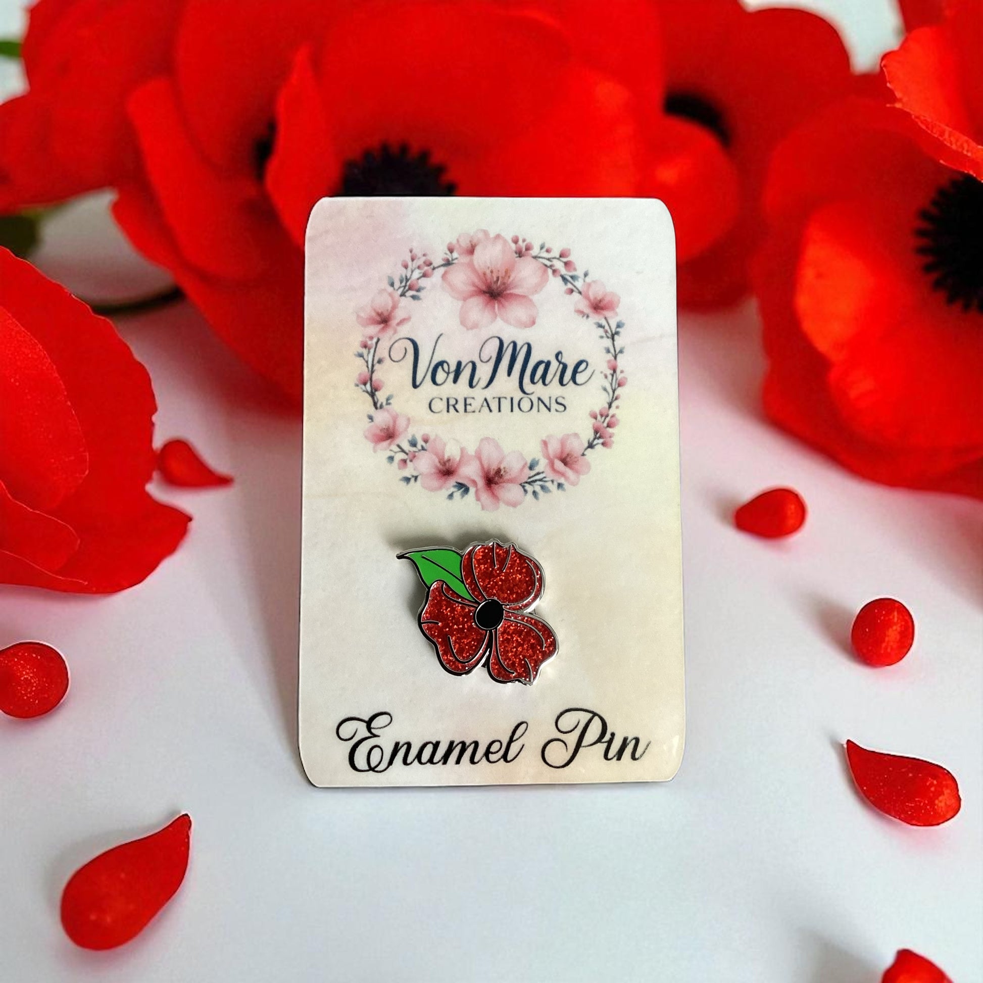 Enamel pin with red flower design on a card labeled 'Von Mare Creations' surrounded by red flowers.