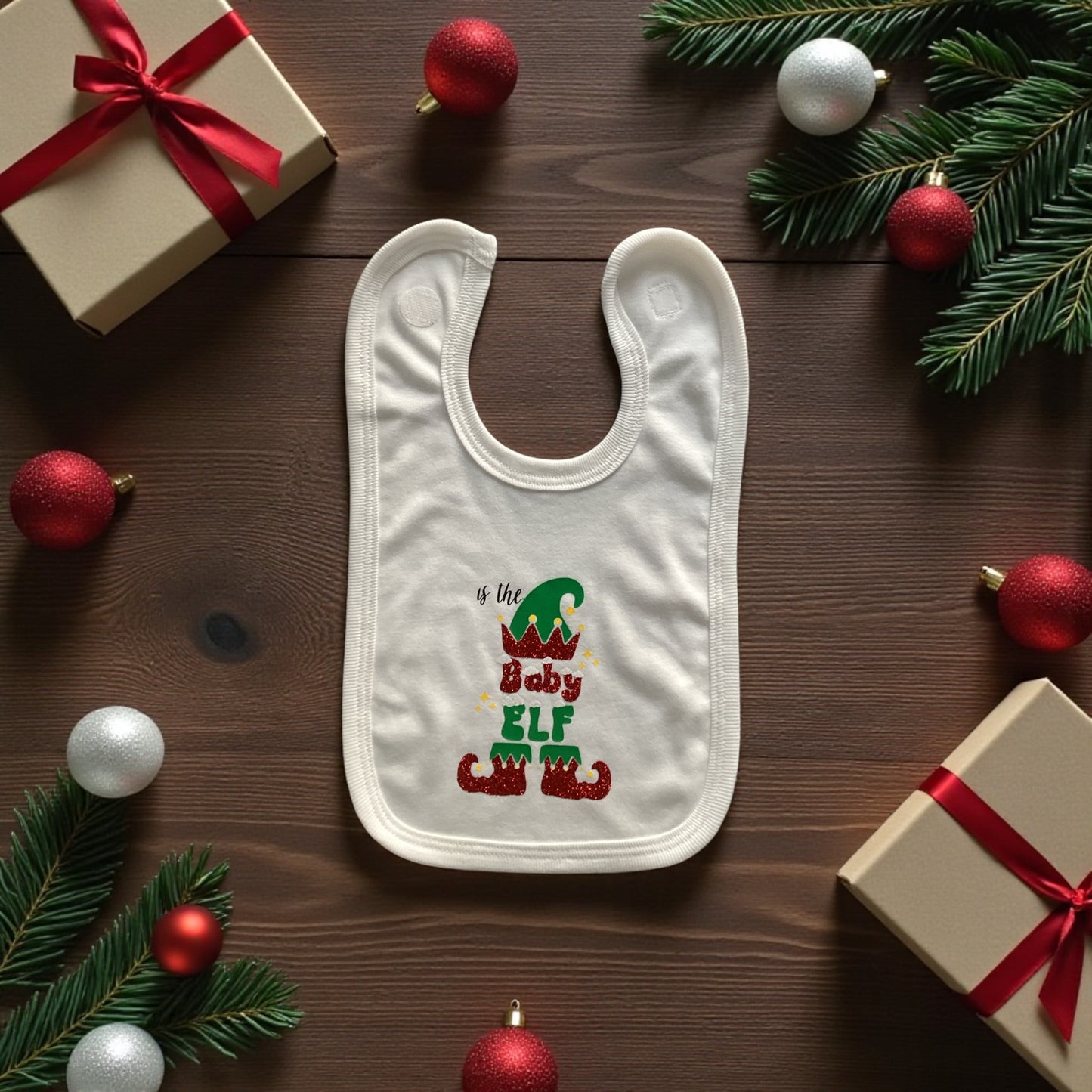 Baby bib with 'Baby Elf' design on a wooden surface with Christmas decorations