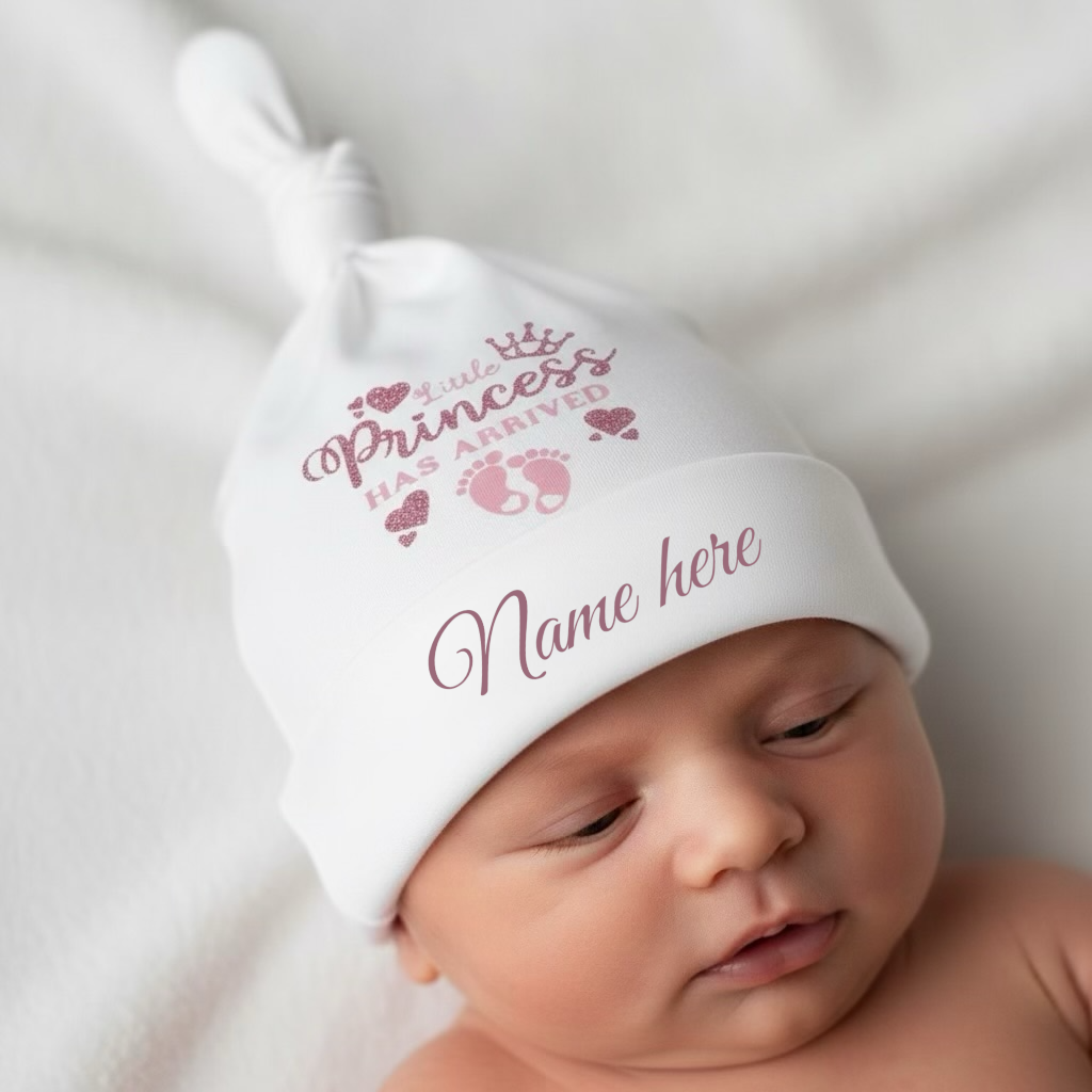 Newborn baby wearing a white hat with personalized text on a soft surface